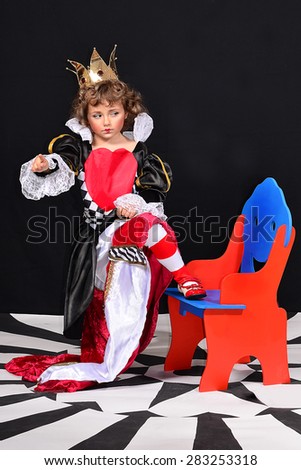 Expressive funny discontented little girl in the image of the Red Queen, with a crown on her head and heart on her dress.