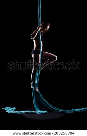 Young woman gymnast with blue gymnastic aerial silks isolated on black
