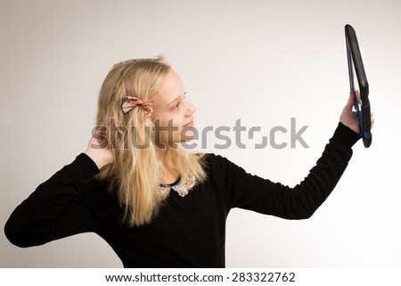 Studio shot of a beautiful blond teenage girl with long hair wearing a bow and a black top taking a selfie.