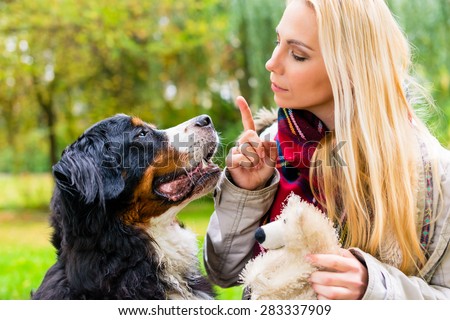 Girl in autumn park training her dog in obedience giving the sit command Royalty-Free Stock Photo #283337909
