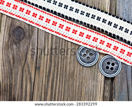 two vintage ribbons with embroidered ornaments andÃ?Â old buttons on a textured surface aged boards