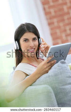 Young woman with tablet and headphones sitting in sofa