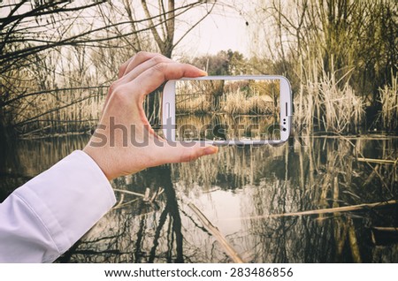 Travel concept - tourist takes a picture of beautiful swamp in summer on smartphone