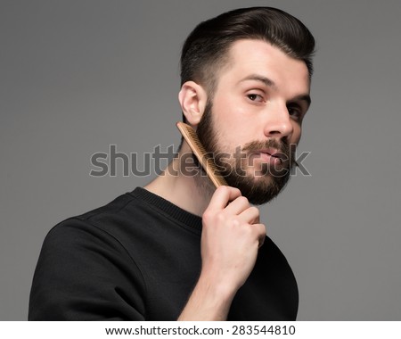 young man comb his beard and moustache on gray background Royalty-Free Stock Photo #283544810