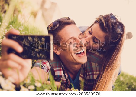 Happy young couple lying at the grass and taking selfie with smart phone