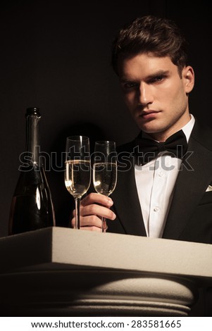Picture of a elegant young business man holding a glass of champagne while looking at the camera.