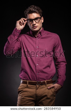 Young fashion man holding his hand in pocket while fixing his glasses.