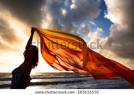 Silhouette of young woman jumping with silk fabric at the beach. Summer vacation concept