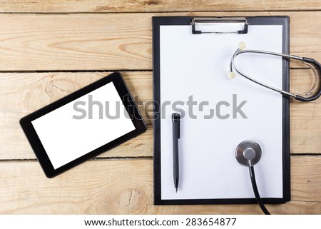 Workplace of a doctor. Tablet, stethoscope, black pen on wooden desk background. Top view