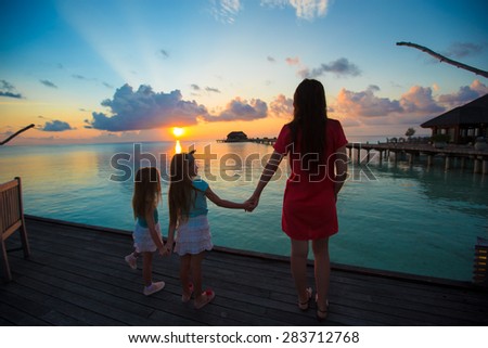 Silhouette of young mother and two her little girls at sunset