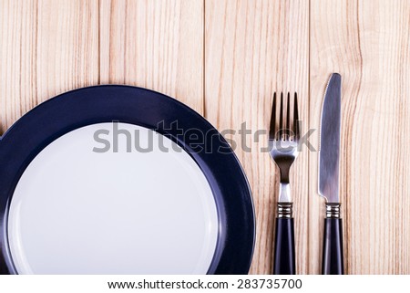 Empty dish, knife and fork and blue napkin on wood table