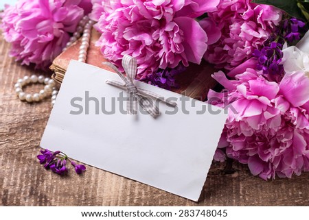 Vintage background. Splendid  pink  peonies flowers and empty tag on aged wooden background. Selective focus. Place for text.