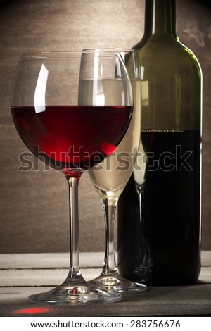 Glasses of red and white wine and bottle on rustic wooden background.