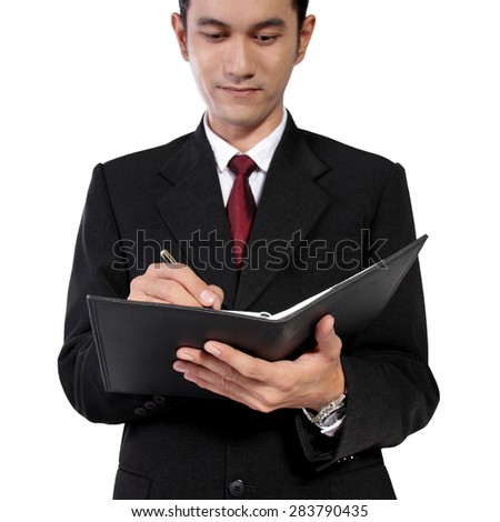 Low angle shot of young Asian man in formal suit writing on a notebook, isolated on white background