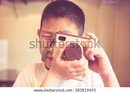 Asian boy holding a wooden camera toy.