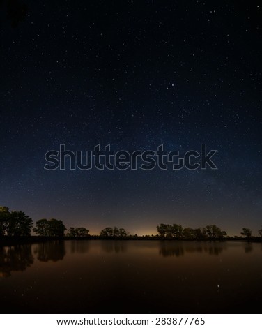 Smooth surface of forest lake on a background of the night sky and the Milky Way.