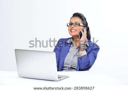 beautiful young woman sitting at office desk and talking on cell phone isolated on white background