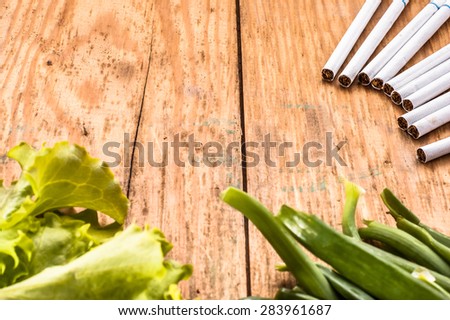 Cigarettes and vegetables arranged on grunge wood background. Concepts of quitting smoking. Choice between healthy lifestyle and unhealthy lifestyle.