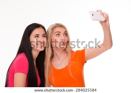 Young pretty blonde and brunette making selfies. Girl orange T-shirt pursing her lips like a duck. 