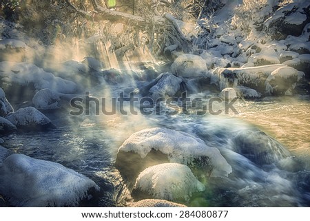 Boiling steamy volcanic river under beams of sunlight surrounded with snow and wintery conditions 