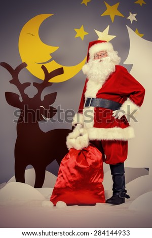 Santa Claus standing with a reindeer in a cartoon fairy snowy forest. Full length portrait.