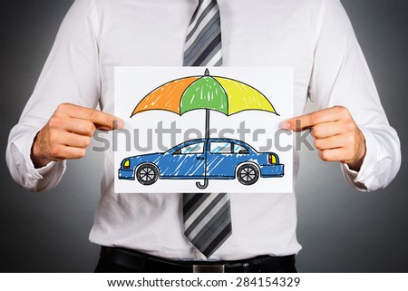 Car insurance concept. Businessman holding white paper with drawn colorful car under safety umbrella. Royalty-Free Stock Photo #284154329