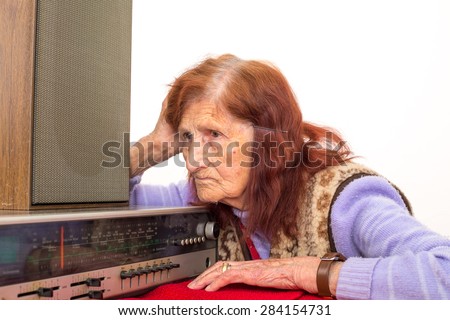 Elderly lady listening attentively to the old radio.