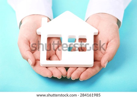 Female hands holding house on color background