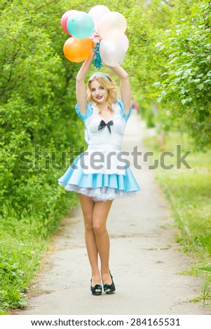 Portrait of a beautiful young blonde woman with long hair dressed as Alice in Wonderland.Girl posing with a big bunch of colorful balloons. Soft focus 