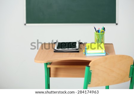 Wooden desk with stationery and tablet in class on blackboard background