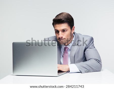 Businessman sitting at the table and working on the laptop  over gray background