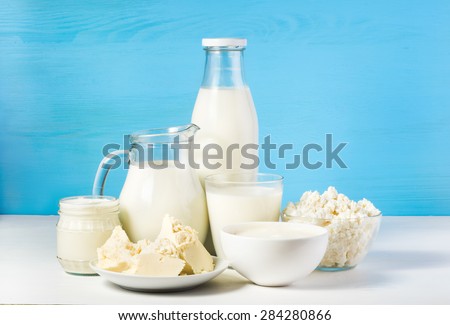 tasty healthy dairy products on a table on a blue background: sour cream in a white bowl, cottage cheese in bowl, cream in a a bank,  butter on a saucer and milk in a jar, glass bottle and in a glass Royalty-Free Stock Photo #284280866