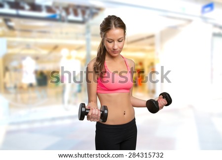 Young woman using dumbbells. Over shopping center background