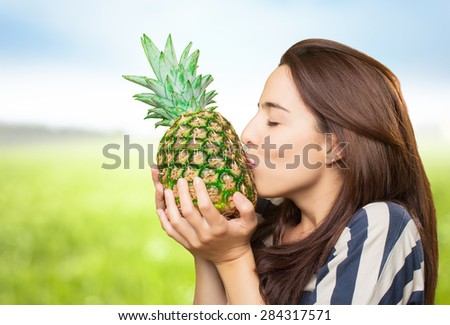 Woman kissing a pineapple. Over nature bokeh background