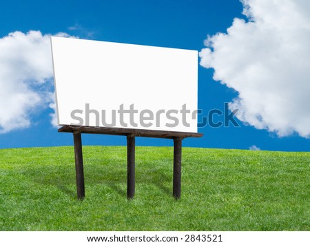 Blank white billboard on a green grassy hill with blue cloudy sky