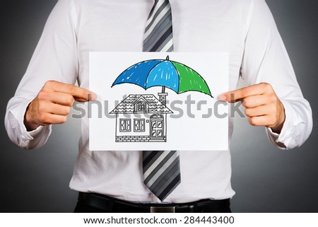 Home insurance concept. Businessman holding paper with drawing of a house under the umbrella.