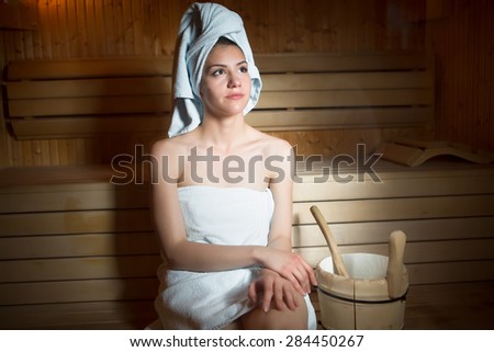 Pretty young  woman sitting relaxed in a wooden sauna.Young woman in white towel sitting in Finnish sauna.