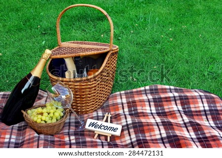 Summer Weekend Picnic With Champagne Wine On The Lawn Close-up Concept. White Signboard With Sign Welcome On The Blanket.