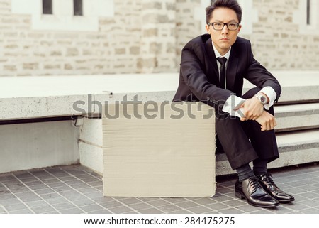 Businessman in a city street sitting next to blank banner