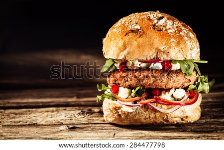 Close Up of Burger Piled High with Fresh Toppings on Whole Grain Artisan Bun, on Rustic Wooden Surface with Dark Background and Copy Space