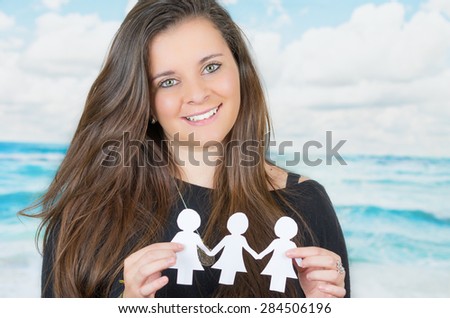 brunette holding an origami paper figure in front of oceanic cloud background while smiling