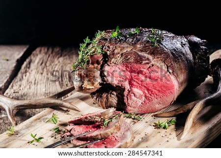 Sliced Rare Venison Roast Seasoned with Fresh Herbs and Served on Wooden Cutting Board with Deer Antlers Royalty-Free Stock Photo #284547341