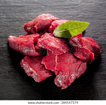 Uncooked lean healthy diced deer steak for a venison goulash with a bay leaf on a textured dark background, close up high angle Royalty-Free Stock Photo #284547374