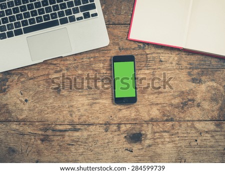 Overhead shot of a laptop, a book and a smart phone with a green screen