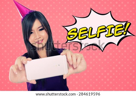 Fun illustration of self shot photo trend. Happy Asian party girl taking self picture with her smartphone camera, with comic styled 'selfie' typography on pink background
