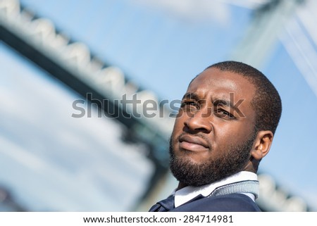 Close up portrait of young confident businessman with Manhattan Bridge in the background. Brooklyn Dumbo Park, New York City.
