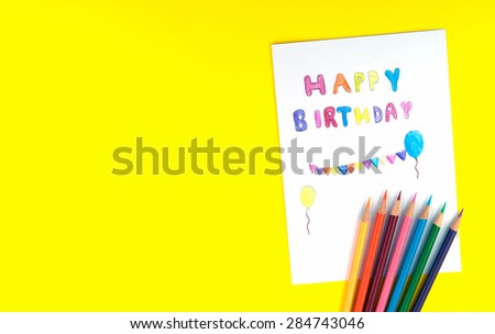 Happy birthday card with many color pencils on yellow background, top view.