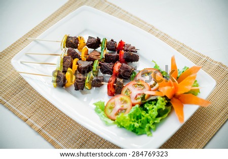 Meat on skewer with grilled vegetables on white plate. Restaurant