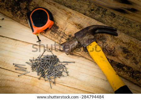 Carpenter equipment include nails hammer and measurement tape placing on the pine wood, focusing on the nails