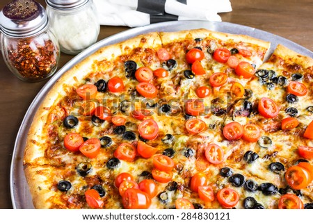 Veggie pizza with olives and cherry tomatoes on the table.